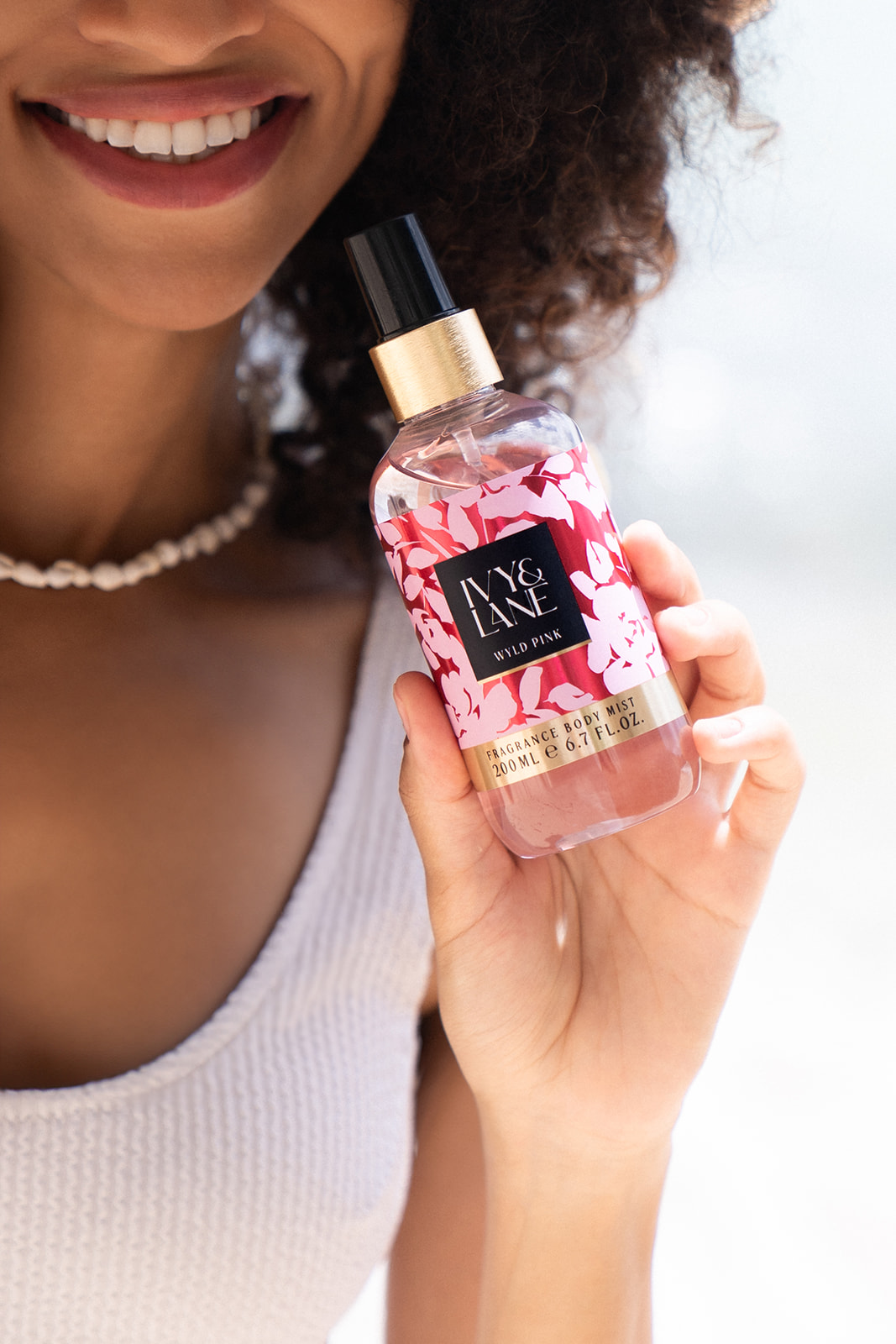 Eine lächelnde Frau hält den Bodymist IVY & LANE Wyld Pink in der Hand